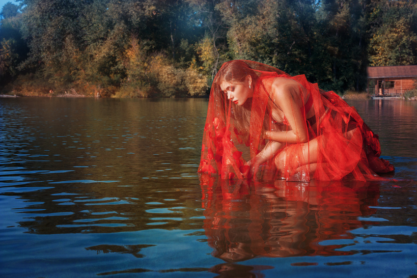 Fairy girl sitting on the water. In her red cape like a veil.